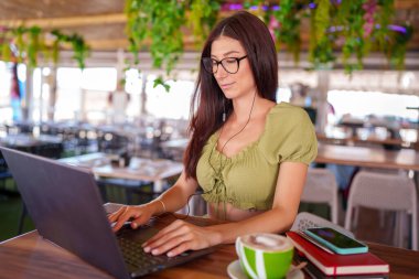 Rahat bir restoranda cappuccino yudumlarken bilgisayar başında çalışan serbest çalışan, görevleri akıllı telefon ve defterle dengeleyen biri.