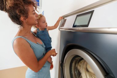 Bebek, çamaşır makinesinin deliğine bozuk para sokuyor. İspanyol kadın çalıştırmak için çamaşır makinesine para atıyor. self-servis çamaşır fabrikası. 