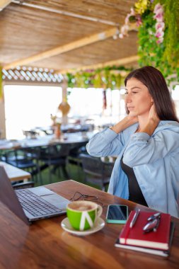 Yoğun bir restoranda uzaktan çalışırken boyun ağrısı çeken serbest çalışan, teslim tarihleriyle uğraşan ve yoğun bir atmosferde stresle başa çıkan serbest çalışan biri.