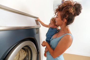 Bebek, çamaşır makinesinin deliğine bozuk para sokuyor. İspanyol kadın çalıştırmak için çamaşır makinesine para atıyor. self-servis çamaşır fabrikası. 
