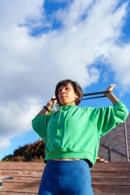 Etkin bir kadın direnç bandı egzersizi yapıyor, dayanıklılık kazanıyor ve açık havada sağlıklı bir yaşam tarzı sürdürüyor.