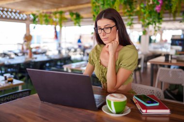 Dizüstü bilgisayarda yazı yazan, öğle arasında kafede çalışırken cappuccino yudumlayan profesyonel kadın serbest yazar.