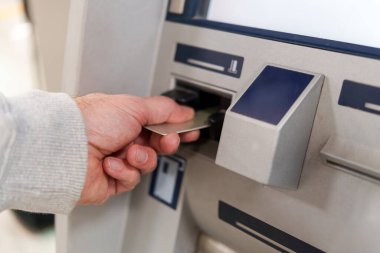 Bir erkeğin bankamatiğe kredi kartı soktuğu görüntüsünü kapat. Fona kolay erişim için hızlı bir finansal işlem yap.