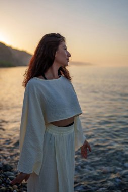 Huzurlu bir kadın okyanus ufkuna bakan renkli günbatımını seyrediyor. Huzurlu bir sahil anı yaşıyor.