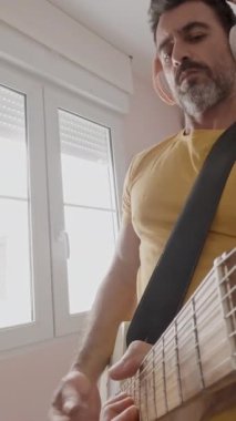 Evde gitar çalan ve kulaklık takan bir adam. 
