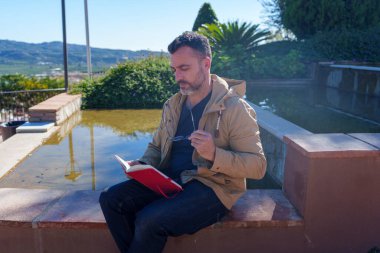 Açık havada günlük okuyan bir adam doğada huzurlu bir anın tadını çıkarırken düşünce ve fikirlere odaklanıyor.