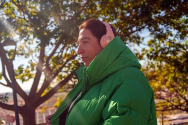 Kulaklıkla müzik dinleyen bir kadın, açık hava keyfi anında yeşil ceketiyle rahat ve rahat hissediyor.