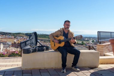 Klasik gitar çalan bir adam, açık gitar çantası manzaralı bahşişlere hazır.