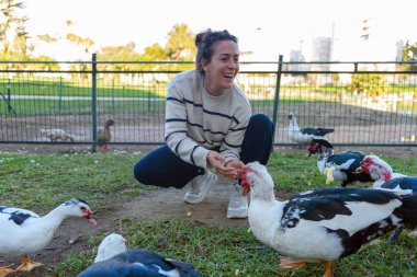 Neşeli kadın bir ördek sürüsüyle meşgul, onları sakin bir açık havada besliyor. Doğanın güzelliğini ve vahşi yaşamla olan bağlantısını kucaklamak