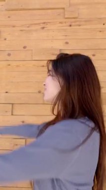 Genç ve güzel Asyalı bir kadın kameraya bakıp dans ediyor ve gülümsüyor. Dışarıda mutluluğu, özgürlüğü ve pozitif enerjiyi ifade ediyor.