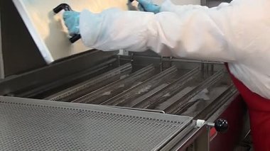 Eldiven giyen biri paslanmaz çelik bir mutfakta büyük, ticari bir fritözü temizler. Öğlen güneşinde yağ tankından metal bir askıyı çıkarıp temizliyorlar..