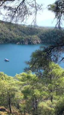 Türkiye 'nin Oludeniz Fethiye bölgesinde huzur dolu bir gün. Beyaz bir tekne, Babadag Dağı 'nın yoğun yeşil ormanları tarafından çerçevelenmiş açık mavi Ege Denizi üzerinde nazikçe yüzer. Güneş ışığı sakin suları aydınlatır..