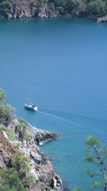 A serene sailboat glides across the dazzling blue Aegean Sea near the Fethiye Oludeniz coast. Rocky shores and distant Babadag Mountain create a beautiful natural panorama.