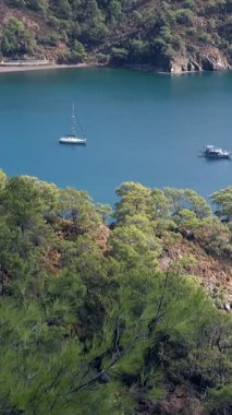 Behold the tranquil Aegean Sea embracing the verdant shores of Fethiye Oludeniz, Turkey. A peaceful sailboat glides on azure waters under the watchful eye of Babadag Mountain.