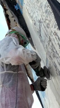 Yetenekli işçiler, geminin gövdesindeki eski boyayı titizlikle çıkararak yeniden boyanması için pürüzsüz ve temiz bir yüzey sağlıyor. İşlem sırasında tozdan ve molozlardan korunmak için güvenlik giysisi giyilir.