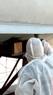 Yetenekli işçiler yoğun tersanedeki geminin gövdesine titizlikle taze boya sürerler. Sabahın erken saatlerinde ışıltı, işçilik ve gemi bakımına olan bağlılığın altını çizer.