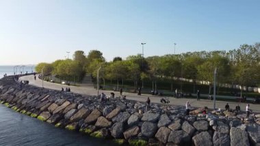 Deniz boyunca geniş yeşil çimenler ve eğlence alanlarının yer aldığı büyük bir sahil kenti parkının sinematik hava aracı görüntüleri. Bu kentsel yeşil alan kamu rahatlığı, şehir planlaması ve açık hava yaşam tarzı projeleri için mükemmeldir..