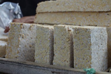 Tempeh 'in yeni kesilmiş bloklarının yakın plan fotoğrafı. Görüntü açık bej soya fasulyesi ve beyaz mantar miselyumuna odaklanmış durumda. Doğal ışıklandırma mayalanmış gıdanın dokusunu ön plana çıkararak otantik bir....