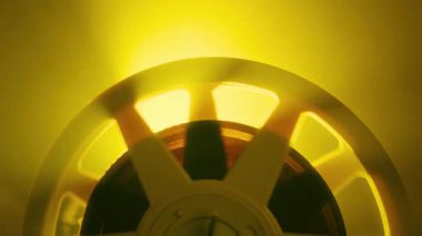 Sarı ışığın aydınlattığı, sıcak ve nostaljik bir atmosfer yaratan dönen bir bant makarasının soyut bir görüntüsü.