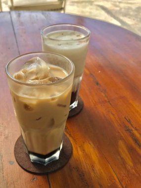 Ahşap masada servis edilen iki ferahlatıcı buzlu kahve sütü. Kafe içeceği, yaz içeceği ve yaşam tarzı içeceği için mükemmel..
