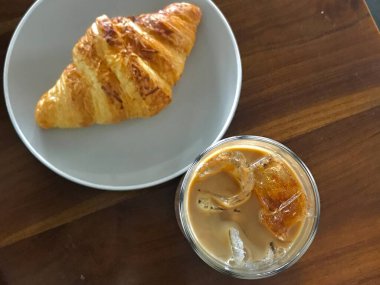 Tahta bir masada servis edilen buzlu kahveyle taze kruvasan eşleştirildi. Basit bir kahvaltı anı, rahat bir kafe yaşam tarzı ve rahat bir sabah atmosferi yakalıyor..