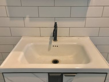 Siyah musluk ve fayans duvarlı beyaz banyo lavabosu