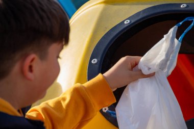 Çocuk naylon poşeti dışarıdaki geri dönüşüm kutusuna koyuyor..