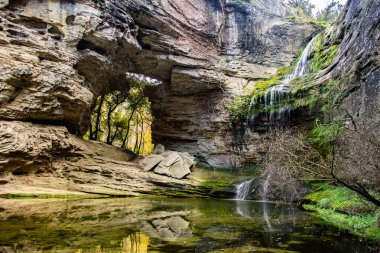 Şelalesi ve sakin göleti olan kayalık bir mağaranın manzarası..