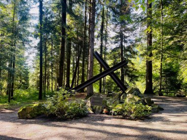 Metal kirişlerin kesişmesi huzurlu bir orman ortamında bir anıt heykel oluşturur.