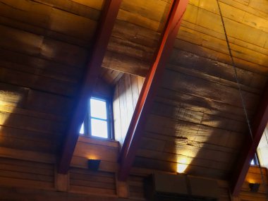 Açıkta duran tahta kirişleri, yalıtımı ve içeri ışık girmesini sağlayan küçük bir pencereyi gösteren tavan arası manzarası.