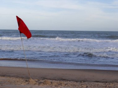 Yalnız bir kırmızı yelken dalgalı bir okyanusta rüzgarı yakalıyor kumlu bir sahilin yanında dalgalar kırılıyor..