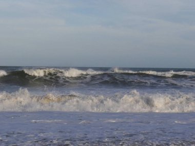 Beyaz köpük ibikli güçlü okyanus dalgaları sessiz ve bulutlu bir gökyüzünün altında kıyıya doğru yuvarlanıyor..