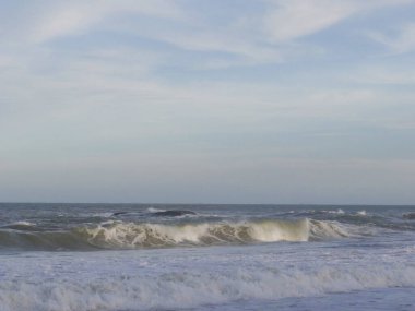 Yumuşak okyanus dalgalarının olduğu sakin bir deniz manzarası sessiz ve bulutlu bir gökyüzü altında kırılıyor..