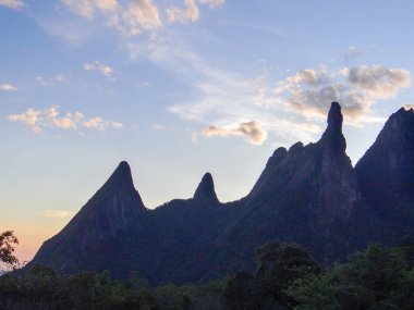 Dramatik sivri dağ zirveleri dağınık bulutlu yumuşak bir günbatımı gökyüzüne karşı siluetlenmiştir..