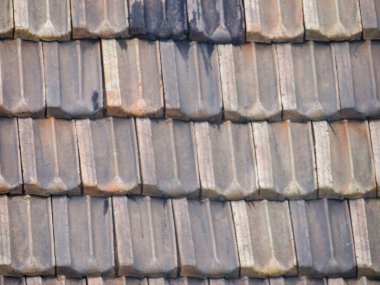 Üst üste binen, yıpranmış kil çatı kiremitlerinin çeşitli renk ve dokulara sahip detaylı bir görünümü.