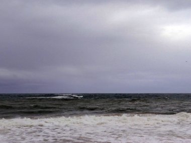 Sert, karanlık okyanus dalgaları karamsar, bulutlu bir gökyüzü altında güneş ışığıyla çarpışıyor..