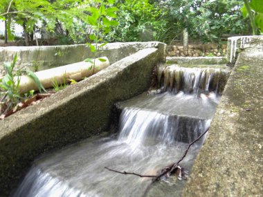 Yeşilliklerle çevrili küçük çağlayanların üzerinden akan suyla dolu insan yapımı bir kanal..