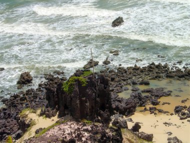 Engebeli, karanlık kayalık bir kıyıya okyanusun köpüklü, beyaz kaplamalı dalgaları çarpar..