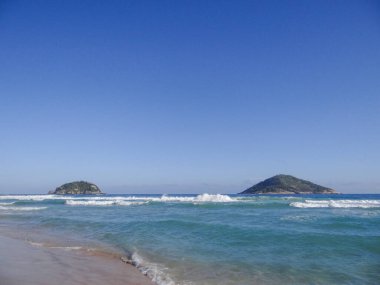 Güzel okyanus manzarası, kumlu sahile vuran dalgalar ve uzaktaki adalar..