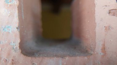 Bir tuğla duvardaki kare açılışının yakın çekim görüntüsü. Yapının dokusunu ve detaylarını gösteriyor.