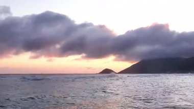 Okyanus dalgaları gün batımında bulutlu gökyüzü ile kıyıya doğru yuvarlanıyor.