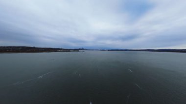 Soğuk su üzerinde sakin bir süzülüş, ince yansımalar ve bulutlu kuzey tonu.