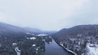 Karlı bir dağ vadisini kesen donmuş bir nehir kıvrımının hava görüntüsü..