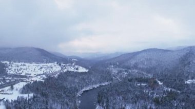 Karlı çam dağları ve soğuk hava tarafından çerçevelenmiş buzlu bir nehrin Drone görüntüsü.