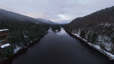 Karlı dağlar arasında akan parlak turkuaz bir nehri takip eden hava manzarası.