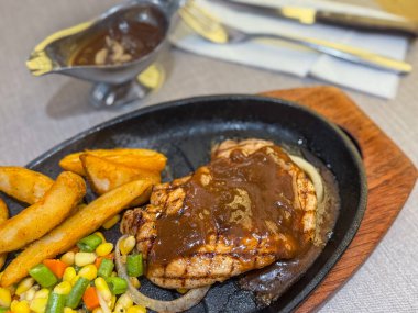 Cızırdayan ızgara tavuk bifteği, altın patates dilimleri, karışık sebzeler, ve sıcak tabakta kalın kahverengi sos. Parlak, renkli restoran yemeği, menüler için ideal, yemek promosyonları ve ticari soslar..