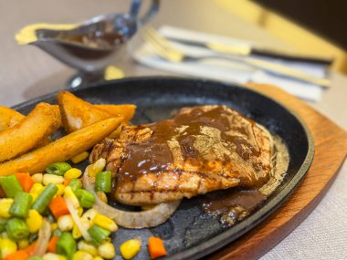 Cızırdayan ızgara tavuk bifteği, altın patates dilimleri, karışık sebzeler, ve sıcak tabakta kalın kahverengi sos. Parlak, renkli restoran yemeği, menüler için ideal, yemek promosyonları ve ticari soslar..