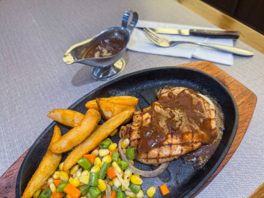 Cızırdayan ızgara tavuk bifteği, altın patates dilimleri, karışık sebzeler, ve sıcak tabakta kalın kahverengi sos. Parlak, renkli restoran yemeği, menüler için ideal, yemek promosyonları ve ticari soslar..