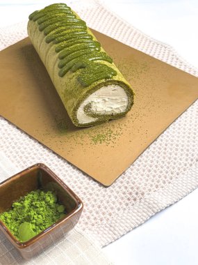 Kremalı kibrit yeşil çay rulo keki, üzeri kibrit jöleli ve kahverengi çarşafta toz çayla kaplı. Yiyecek fotoğrafçılığı kullanımı için yumuşak arkaplan ve sığ alan derinliği.