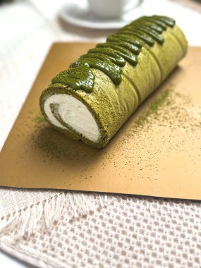 Kremalı kibrit yeşil çay rulo keki, üzeri kibrit jöleli ve kahverengi çarşafta toz çayla kaplı. Yiyecek fotoğrafçılığı kullanımı için yumuşak arkaplan ve sığ alan derinliği.